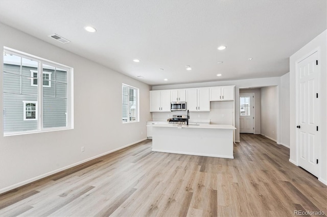 kitchen with a wealth of natural light, white cabinetry, an island with sink, and stainless steel appliances