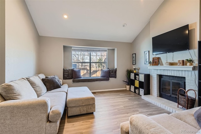 living room with vaulted ceiling, a brick fireplace, and light hardwood / wood-style flooring