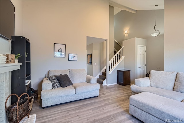 living room featuring a brick fireplace, beam ceiling, high vaulted ceiling, and light wood-type flooring