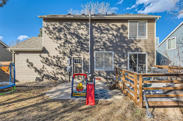 back of property with a trampoline and a deck