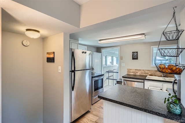 3655 Zenobia St, Denver, CO 80212 - kitchen with appliances with stainless steel finishes, dark countertops, backsplash, light wood finished floors, and white cabinetry