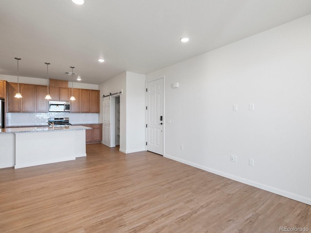 kitchen with decorative backsplash, a barn door, light stone countertops, decorative light fixtures, and stainless steel appliances