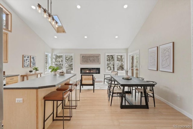 dining space featuring a skylight, baseboards, light wood-style flooring, high vaulted ceiling, and recessed lighting