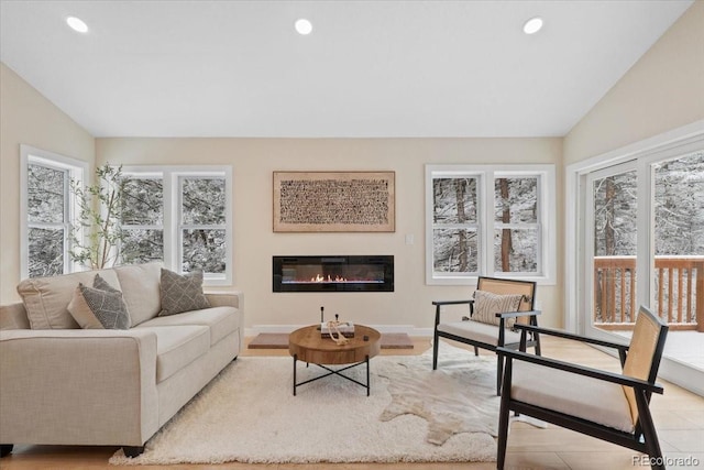 living area with lofted ceiling, baseboards, a glass covered fireplace, and recessed lighting