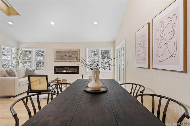 dining area with lofted ceiling, recessed lighting, wood finished floors, and a glass covered fireplace