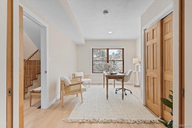 office space featuring light wood-style floors, baseboards, and a textured ceiling