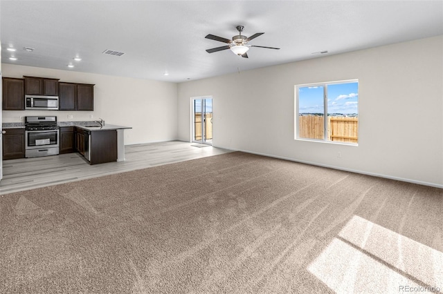 unfurnished living room featuring ceiling fan, light colored carpet, and sink