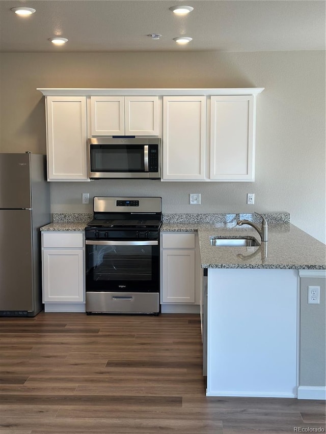 kitchen with appliances with stainless steel finishes, a peninsula, wood finished floors, white cabinets, and a sink