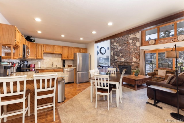 kitchen with light stone counters, a peninsula, appliances with stainless steel finishes, light wood-type flooring, and backsplash