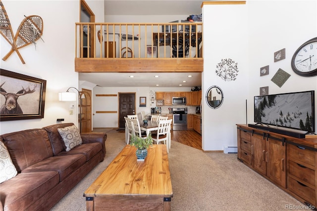 living room featuring baseboard heating, baseboards, a towering ceiling, and light carpet