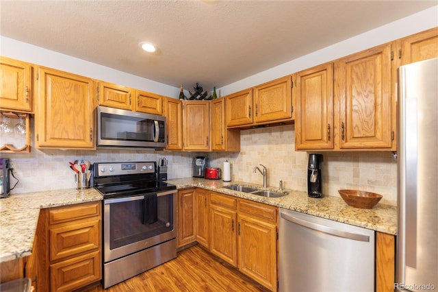 kitchen with light stone countertops, light wood finished floors, a sink, stainless steel appliances, and tasteful backsplash