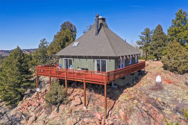 back of property with a chimney, a deck, and a shingled roof