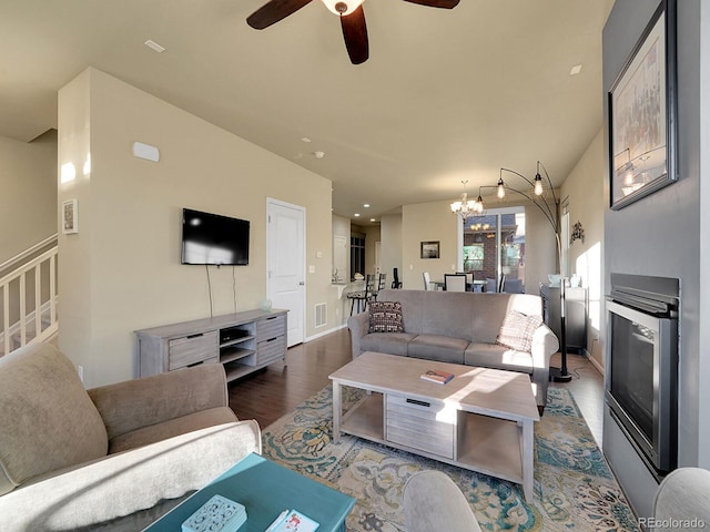 living area featuring baseboards, visible vents, a glass covered fireplace, wood finished floors, and ceiling fan with notable chandelier