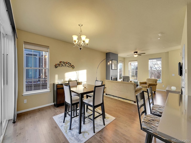 dining area featuring a glass covered fireplace, baseboards, light wood finished floors, and ceiling fan with notable chandelier