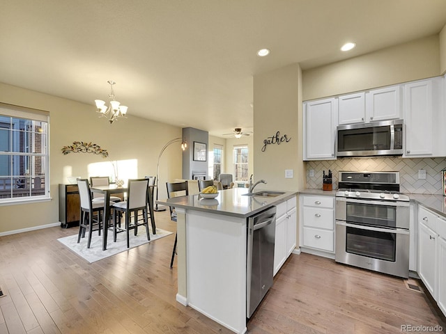 kitchen with decorative backsplash, a peninsula, stainless steel appliances, light wood-style floors, and a sink