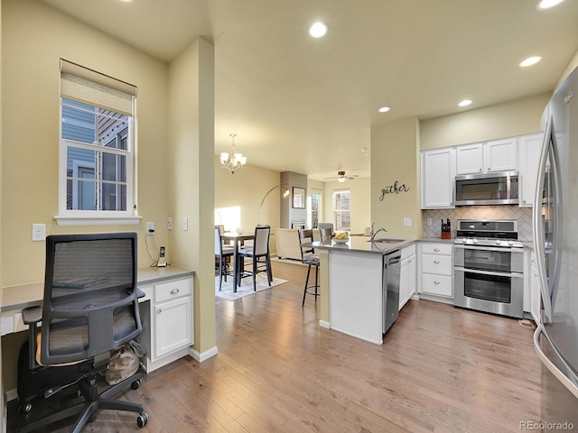 kitchen featuring stainless steel appliances, tasteful backsplash, a sink, wood finished floors, and a peninsula