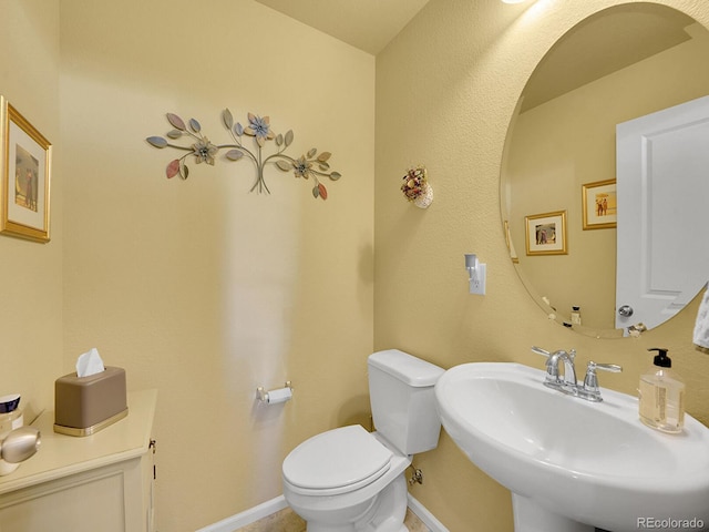 half bathroom with a sink, toilet, and baseboards