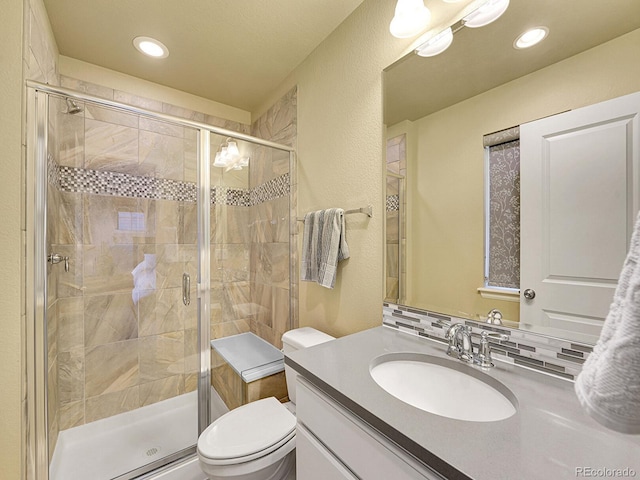 full bath featuring a textured wall, vanity, toilet, and a shower stall