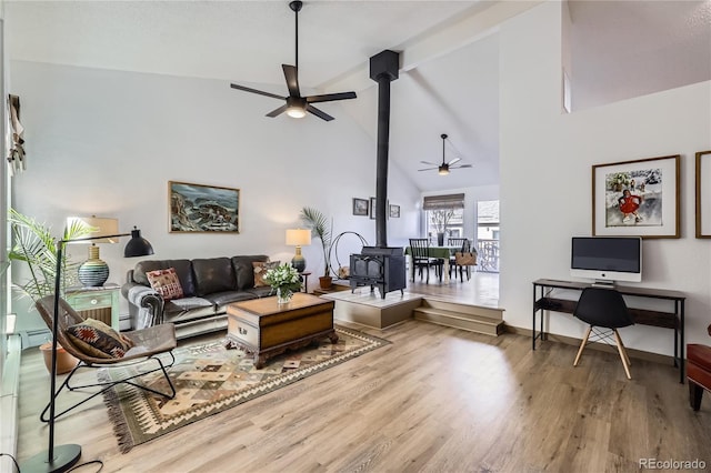 living room with a wood stove, ceiling fan, wood finished floors, high vaulted ceiling, and baseboards