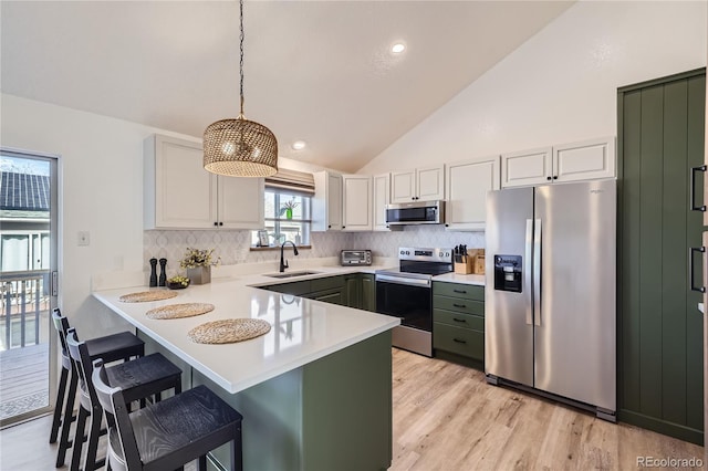 kitchen featuring a breakfast bar area, stainless steel appliances, light countertops, a sink, and a peninsula