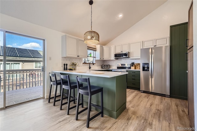 kitchen featuring a peninsula, a breakfast bar, light countertops, appliances with stainless steel finishes, and backsplash