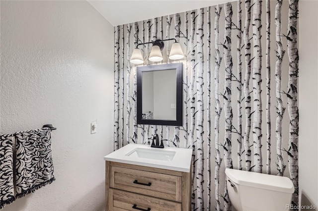 half bathroom with a textured wall, vanity, and toilet