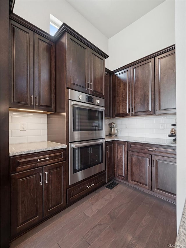 6970 E Lake Dr, Centennial, CO 80111 - kitchen with dark brown cabinets, light stone countertops, stainless steel double oven, dark wood finished floors, and decorative backsplash