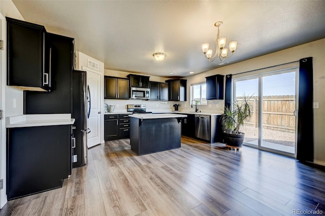 kitchen with pendant lighting, a kitchen island, stainless steel appliances, and light hardwood / wood-style flooring