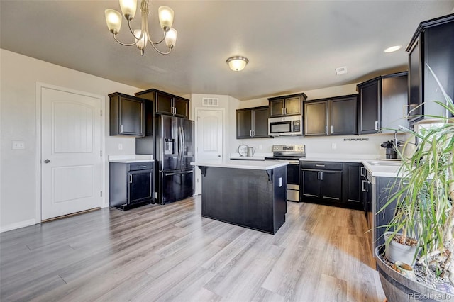 kitchen featuring appliances with stainless steel finishes, light wood-type flooring, a chandelier, a kitchen island, and hanging light fixtures