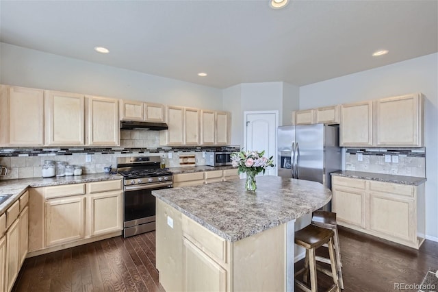 kitchen featuring dark hardwood / wood-style floors, decorative backsplash, appliances with stainless steel finishes, a kitchen island, and a kitchen bar