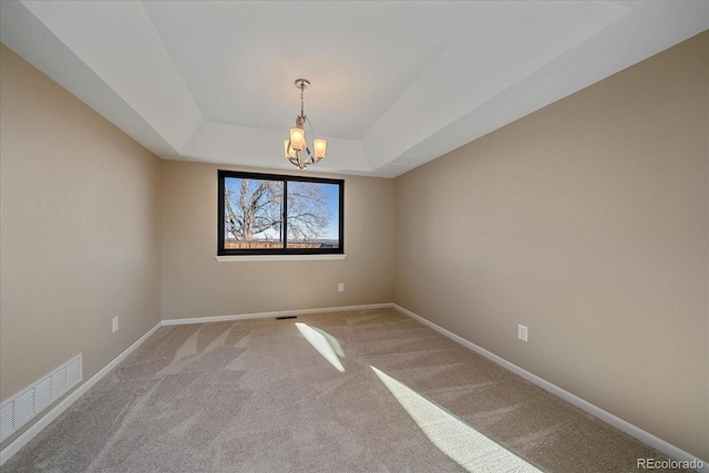 carpeted spare room with a notable chandelier and a raised ceiling