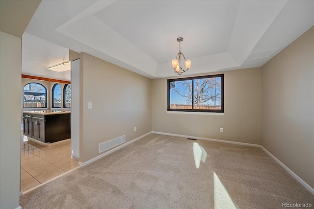 spare room featuring a notable chandelier, light colored carpet, and a tray ceiling