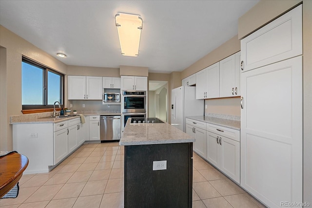 kitchen with light stone countertops, stainless steel appliances, a kitchen island, white cabinetry, and sink