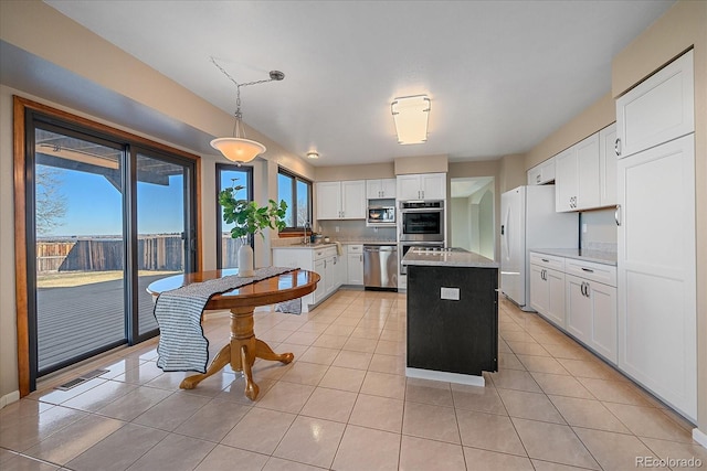 kitchen featuring appliances with stainless steel finishes, light tile patterned floors, a kitchen island, white cabinets, and decorative light fixtures