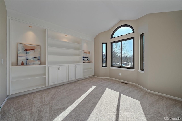 spare room featuring light carpet, vaulted ceiling, and built in features