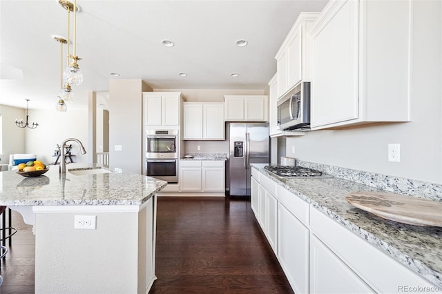 kitchen featuring dark wood-style flooring, light stone counters, white cabinets, appliances with stainless steel finishes, and a sink