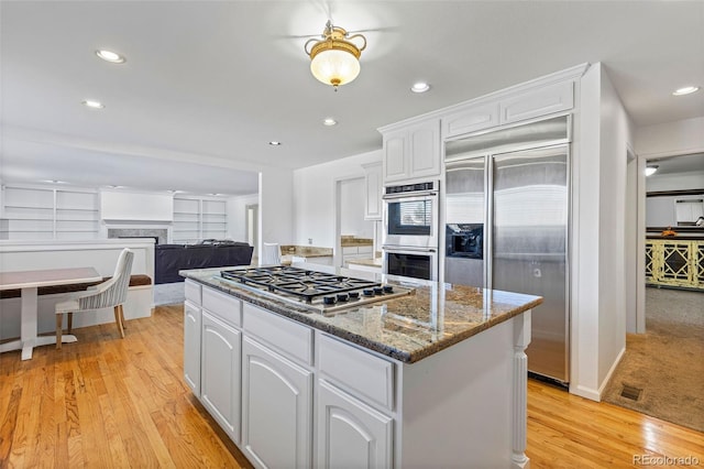 kitchen featuring stainless steel appliances, dark stone counters, light wood-type flooring, and white cabinets