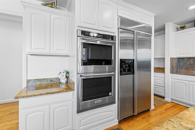 kitchen with tasteful backsplash, appliances with stainless steel finishes, light hardwood / wood-style floors, white cabinets, and dark stone countertops