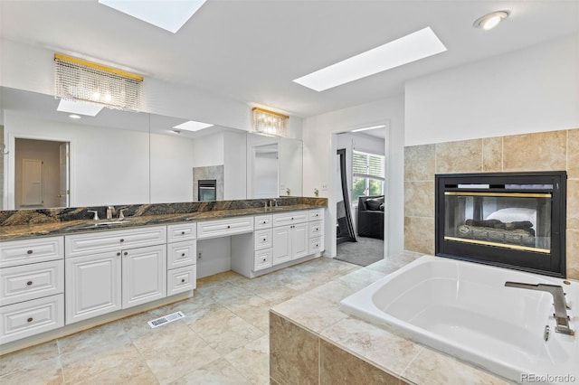 bathroom with vanity, a fireplace, tiled bath, and a skylight