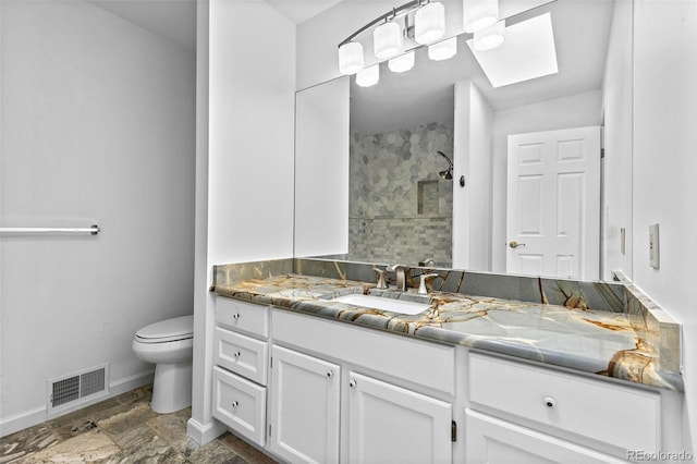 bathroom with vanity, toilet, a tile shower, and a skylight