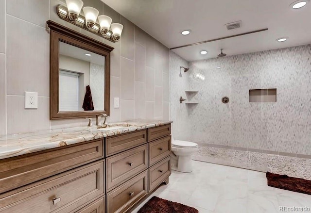 bathroom featuring vanity, toilet, tile walls, and tiled shower