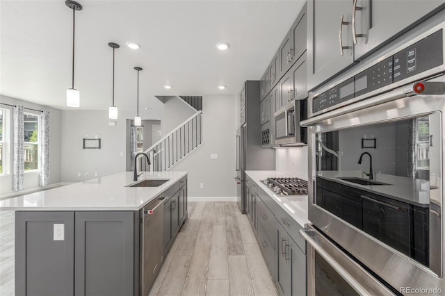 3338 Ireland Moss St, Castle Rock, CO 80109 - kitchen featuring gray cabinetry, appliances with stainless steel finishes, light wood finished floors, a center island with sink, and light countertops