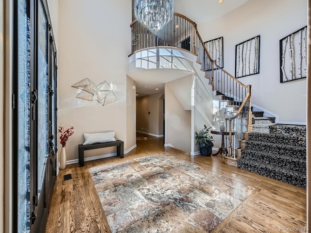 entryway with a notable chandelier, a towering ceiling, wood finished floors, baseboards, and stairs