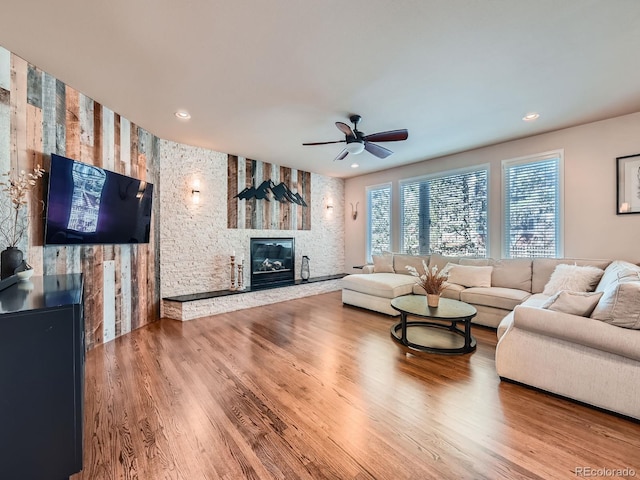 living area featuring recessed lighting, a ceiling fan, wood finished floors, and a stone fireplace