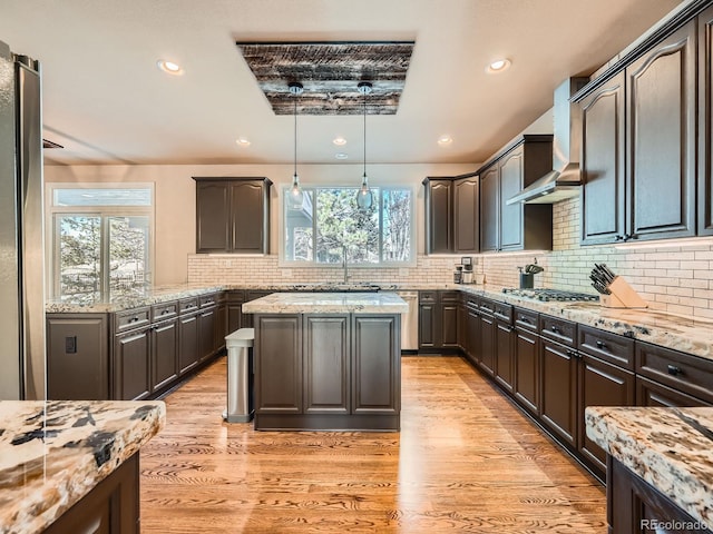 kitchen with light stone counters, decorative light fixtures, dark brown cabinetry, and light wood finished floors