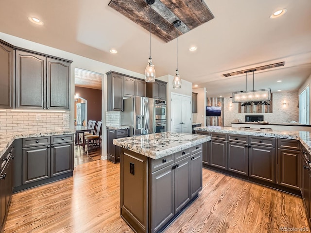 kitchen featuring stainless steel appliances, hanging light fixtures, light wood-type flooring, a center island, and tasteful backsplash