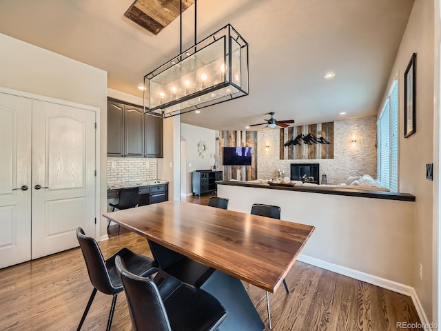 dining space with a large fireplace, light wood-style flooring, baseboards, and ceiling fan