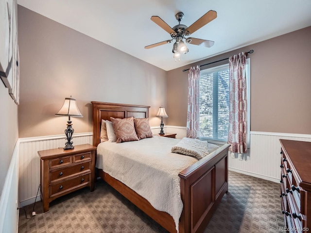 bedroom featuring ceiling fan, dark colored carpet, and wainscoting