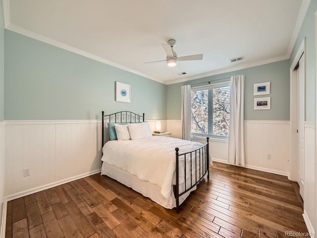 bedroom with ornamental molding, dark wood-type flooring, wainscoting, and visible vents