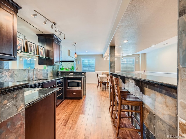 kitchen featuring dark stone counters, wine cooler, stainless steel microwave, decorative light fixtures, and light wood-type flooring